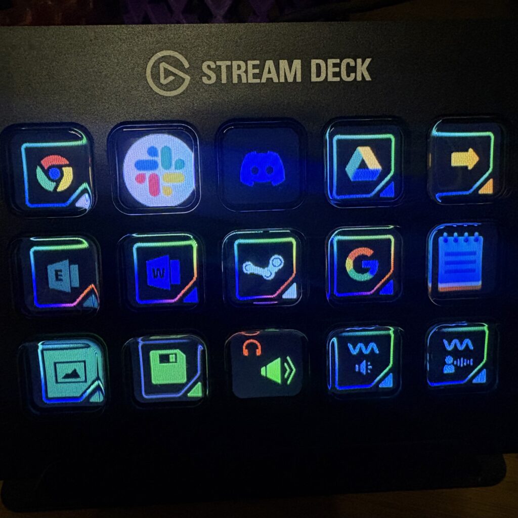An Elgato Stream Deck with 15 illuminated LCD buttons displaying app shortcut icons including Google Chrome, Slack, Discord, Google Drive, Microsoft Word, Steam, and audio control buttons, glowing with RGB lighting against a black surface.
