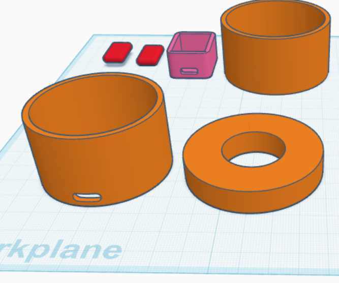 A Tinkercad 3D design workspace displaying several orange cylindrical containers, a pink small box, two red rectangular shapes, and an orange torus (donut-shaped) object arranged on a blue grid workplane.